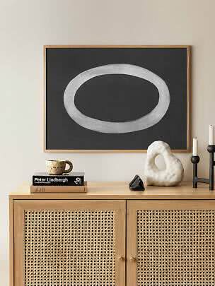 Affiche abstraite encadrée avec forme ovale blanche sur fond noir au-dessus d'un meuble en bois clair