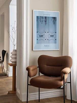 Gerahmtes Paris-Poster mit hellblauer Tür hängt über einem braunen Sessel in hellem Raum