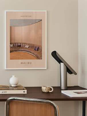 Poster di architettura incorniciato sopra una scrivania con lampada, vaso, tazza e libri