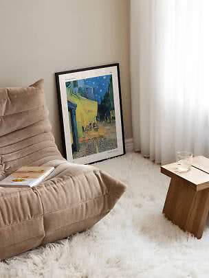Affiche encadrée de Van Gogh posée contre un mur, près d’un fauteuil beige et d’une table en bois