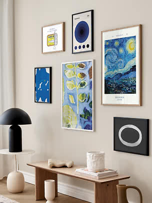 Billedvæg med indrammede kunstplakater over træbænk og sort bordlampe