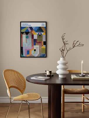 Gerahmtes farbiges Paul-Klee-Poster an beiger Wand über dunklem Esstisch mit weißer Vase und Kerze.