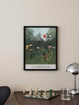 Indrammet Henri Rousseau-plakat med junglemotiv hængende over et bord med skakbræt og lampe