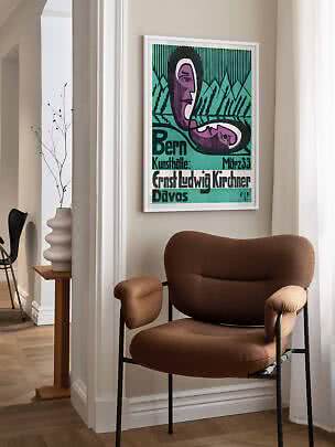 Framed colorful art poster above a brown lounge chair in a bright room corner