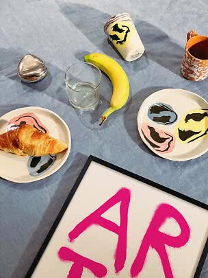 Frukostscen med croissant, banan, glas, mugg och konstnärliga tallrikar på blå duk