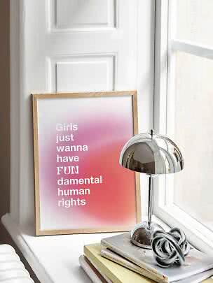 Indrammet lyserød plakat med tekst på vindueskarm ved siden af kromlampe og bøger