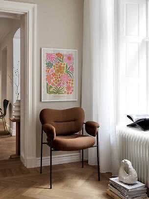 Fauteuil rembourré brun à côté d’une affiche florale colorée dans une pièce lumineuse