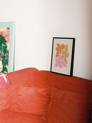Affiche florale encadrée posée contre le mur au-dessus d’un canapé rouille