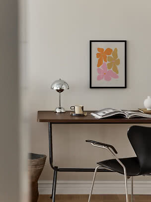 Bureau moderne en bois avec lampe chromée, tasse, livre ouvert et affiche florale