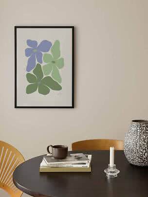 Lámina floral enmarcada con flores abstractas azules y verdes en pared clara sobre mesa negra