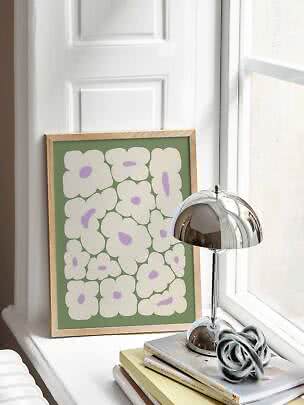 Gerahmtes Blumenposter mit weißen Blumen auf grünem Hintergrund auf einer Fensterbank neben Chromlampe