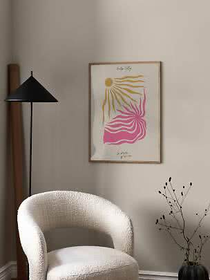 Framed abstract poster with yellow sun and pink waves above a white armchair beside a black floor lamp