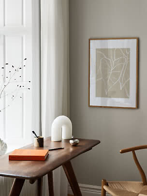Scrivania minimalista con libro, vaso e stampa botanica incorniciata vicino alla finestra