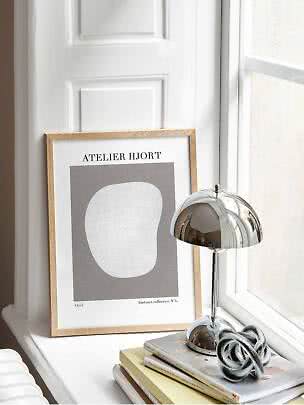 Lampe de table chromée sur une pile de livres près d’une affiche abstraite encadrée