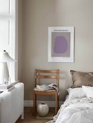 Schlafzimmerecke mit abstraktem Poster, Holzstuhl mit Magazin, weißem Bett und Lampe am Fenster