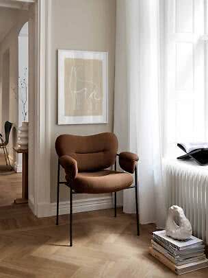 Fauteuil rembourré brun à pieds noirs dans un coin lumineux, près d'une fenêtre.