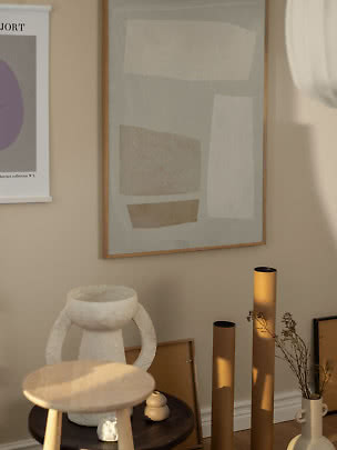 Lámina abstracta enmarcada en pared beige sobre una mesa con jarrones decorativos