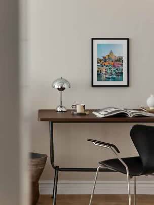 Desk with chrome lamp, mug and open book beneath framed colorful harbor print
