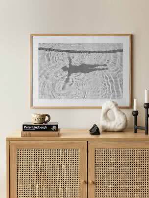 Framed black-and-white art print of a swimmer’s shadow in water above a wooden sideboard with decor