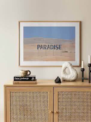 Poster incorniciato con paesaggio desertico e scritta "PARADISE" sopra un mobile in legno.