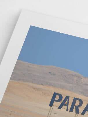 Primo piano di una stampa artistica con paesaggio desertico, cielo azzurro e testo parziale in basso