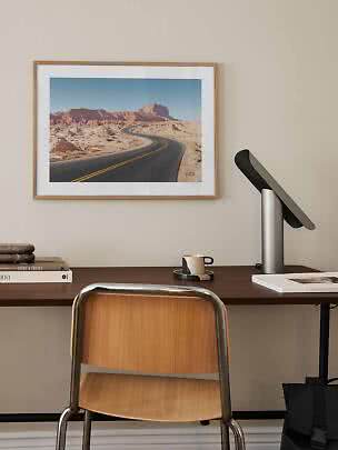 Escritorio con silla, lámpara y cuadro enmarcado de carretera en el desierto