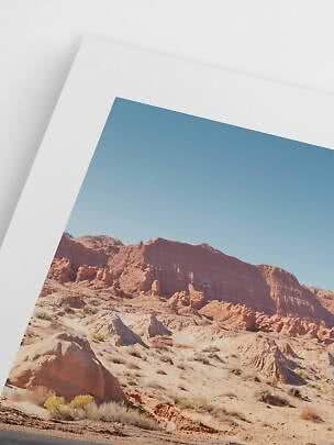 Primer plano de una lámina enmarcada de paisaje desértico con rocas rojas y cielo azul