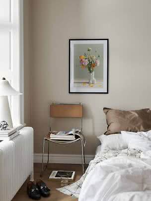Soveværelse med seng, stol og indrammet blomsterplakat på beige væg