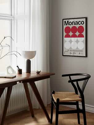 Gerahmtes Monaco-Poster mit roten und weißen Kreisen an der Wand über Schreibtisch und schwarzem Stuhl