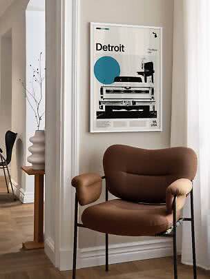 Indrammet Detroit-plakat med pickupmotiv hænger over brun lænestol i lyst hjørne