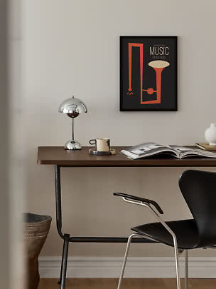Desk with chrome lamp, mug, open book and framed music poster on a light wall