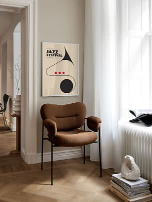 Brun polstret stol med sorte ben ved siden af et jazzfestival-print i et lyst hjørne