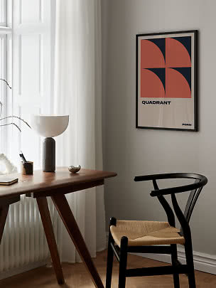 Indrammet grafisk plakat med orange og mørkeblå former over et skrivebord ved vinduet