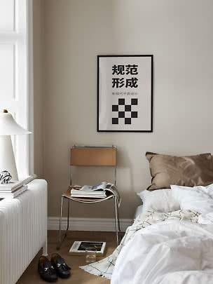 Minimalistisches Schlafzimmer mit Bett, Stuhl, Lampe und Schwarzweiß-Poster an beiger Wand