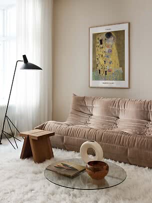 Inramad poster av Klimts The Kiss ovanför en beige soffa i ett ljust vardagsrum