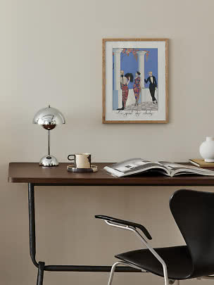 Modern desk with chrome lamp, mug, open book, and framed art print on a beige wall