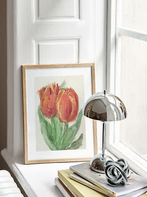 Indrammet tulipanplakat på vindueskarm ved siden af kromlampe og stak bøger