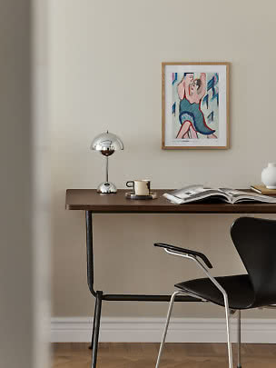 Scrivania in legno scuro con lampada cromata, tazza, libro aperto e quadro su parete beige
