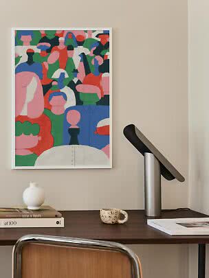 Gerahmter farbiger Kunstdruck mit abstrakten Figuren über einem Schreibtisch.