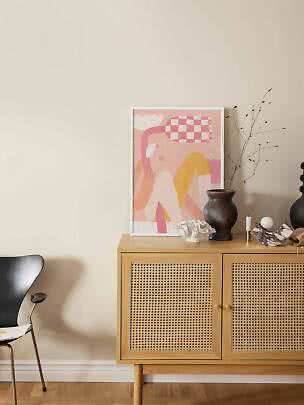 Abstract pink and yellow poster on an oak cabinet with woven doors and a dark vase.