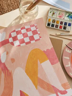 Painting table with abstract pink artwork, watercolor palette, brushes and glass jar of water