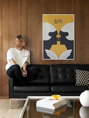 Person sitzt auf schwarzem Sofa vor Holzwand unter gelb-schwarzem abstraktem Poster
