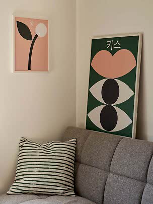 Dos pósters abstractos sobre un sofá gris con cojín de rayas verdes en un rincón luminoso
