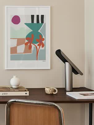 Indrammet abstrakt plakat med vase og blomster over et skrivebord med lampe og bøger