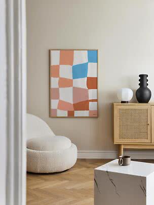 Abstract colorful framed wall art above an armchair beside a cabinet in a modern living room