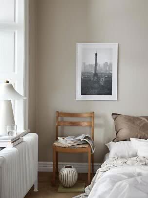 Schlafzimmer mit Bett, Holzstuhl mit Magazin und gerahmtem Eiffelturm-Bild an der Wand