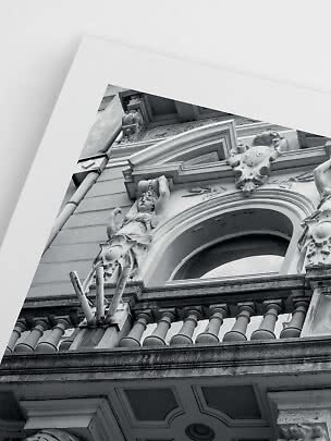Sort-hvidt foto af udsmykket bygning med balkon, buevindue og statue set nedefra