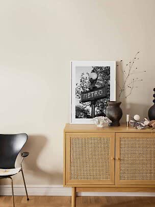 Mobile in legno con ante intrecciate, vaso e stampa Metro in bianco e nero su parete beige