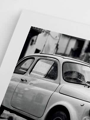 Black-and-white print of a classic small car photographed close up in the rain