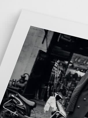 Black-and-white photo print showing a street scene with scooters and a person in a dark coat